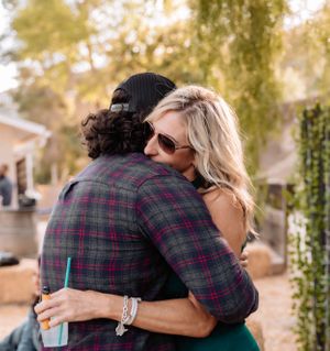 A couple shares a tender moment at an outdoor gathering with decorative lights and trees.