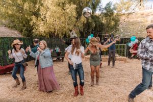 Dancers performing coordinated country line dance moves at an outdoor event with string lights.