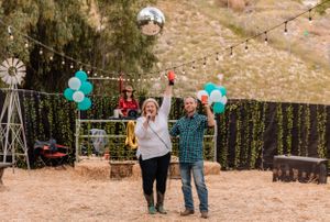 Outdoor party setup with teal balloons and string lights among trees.