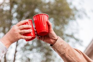 Hands raised holding red plastic cups in a celebratory toast.