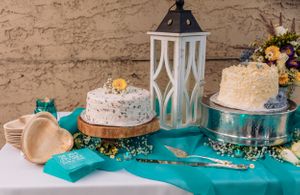 Dessert table decorated with white lanterns and cakes on turquoise tablecloth.