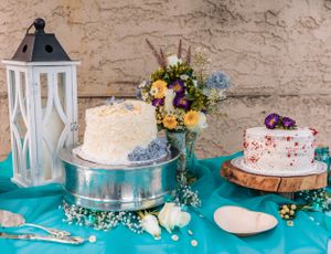 Wedding cake display featuring multiple tiers and white decorative lanterns on turquoise tablecloth.