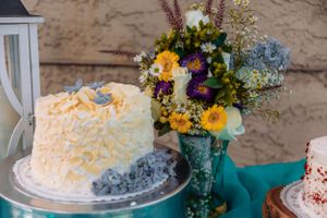 Rustic dessert table display with white cakes and turquoise accents against a textured wall.