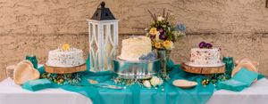 Elegant cake display featuring white frosted desserts and turquoise table settings in a rustic venue.