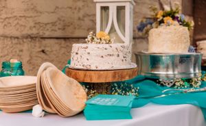 Rustic dessert table setup with white cakes and vintage decor elements on turquoise linens.
