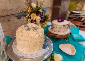 White frosted cakes adorned with yellow flowers displayed on wooden cake stands with turquoise accents.