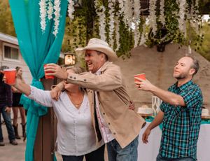 Guests celebrate with drinks under a decorated outdoor pergola with teal accents.