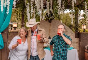 Party guests share laughs and drinks at an outdoor gathering with teal and floral decorations.