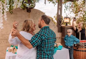 Festive outdoor celebration with guests enjoying drinks under floral and teal decorations.
