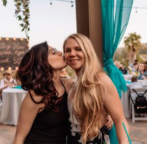 Friends sharing joyful laughter at an outdoor event with turquoise curtains.
