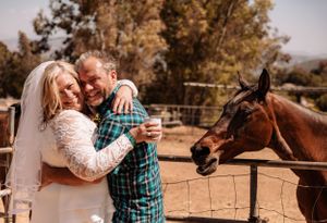 A romantic moment captured at a ranch with horses visible in the background.