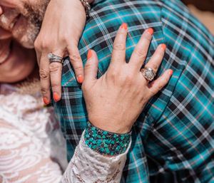 Detail shot of hands with rings against a turquoise plaid shirt pattern.