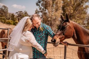 A wedding couple shares a moment at a ranch with horses nearby.