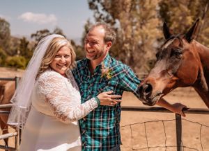 A rustic outdoor wedding scene with horses and wooden fence in background.