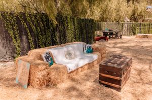 Rustic outdoor venue setup with wooden elements and hay bales under tree cover.