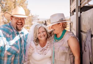 Cheerful gathering of people in western wear sharing laughs by a wooden structure.