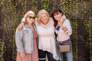 Friends posing casually against vine-covered wall in coordinated outfits of white, denim and pink.