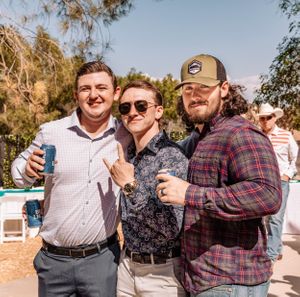 Casual outdoor gathering with people sharing drinks and laughs in western-themed clothing.