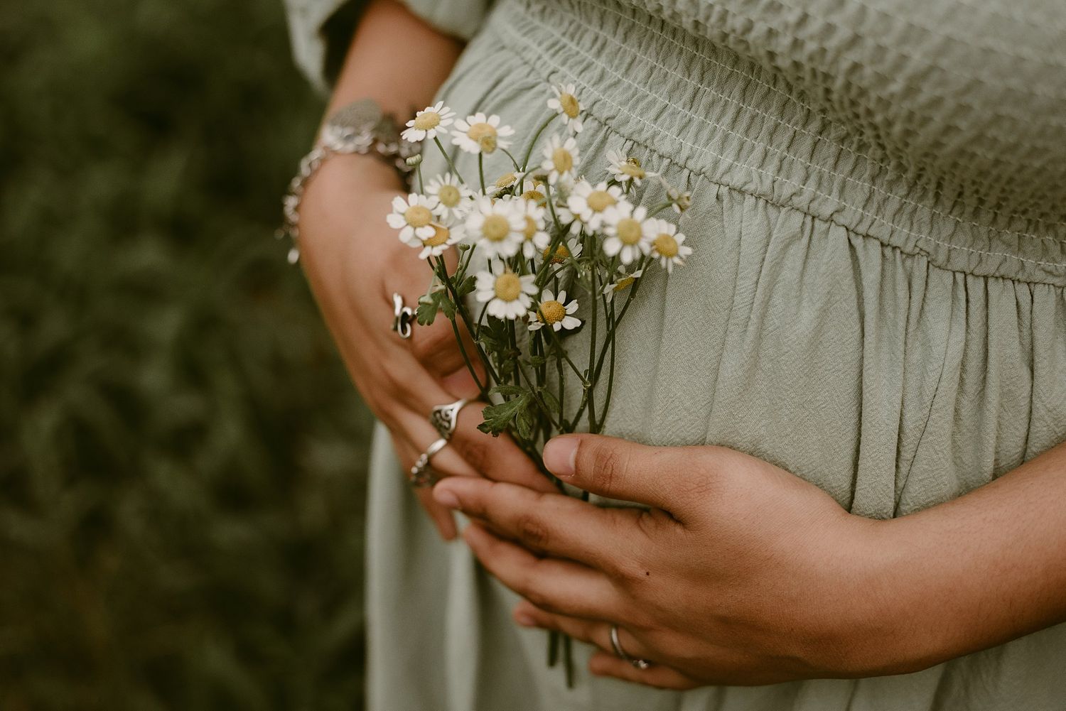 Close-up of hands holding delicate wildflowers against grey fabric.