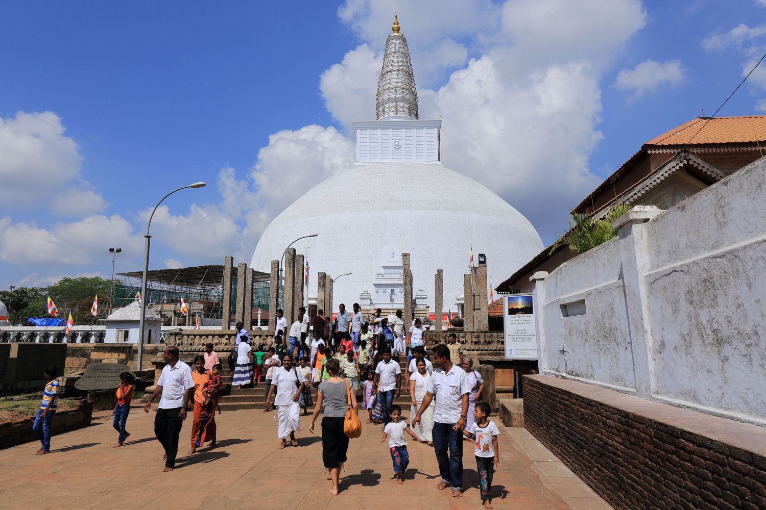 White Buddhist stupa temple with visitors climbing stairs under blue sky.