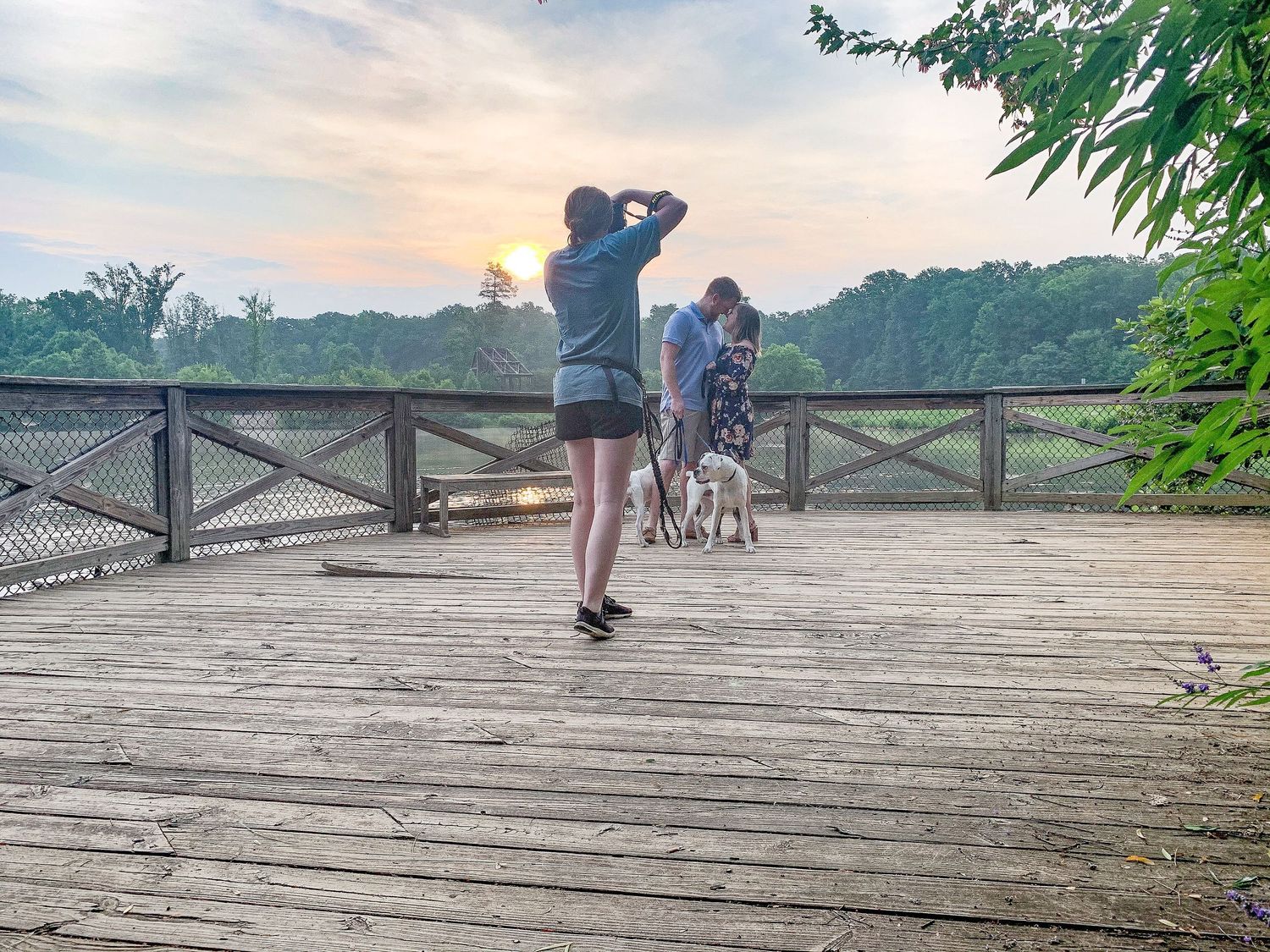 Wooden dock stretches across a scenic lake at sunset with silhouettes of people enjoying the peaceful morning view.