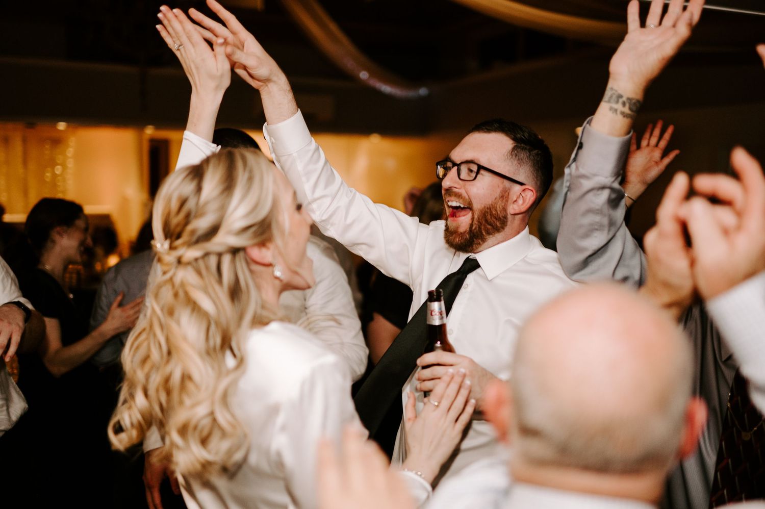 Enthusiastic dancers with raised arms celebrating at a lively indoor wedding reception.
