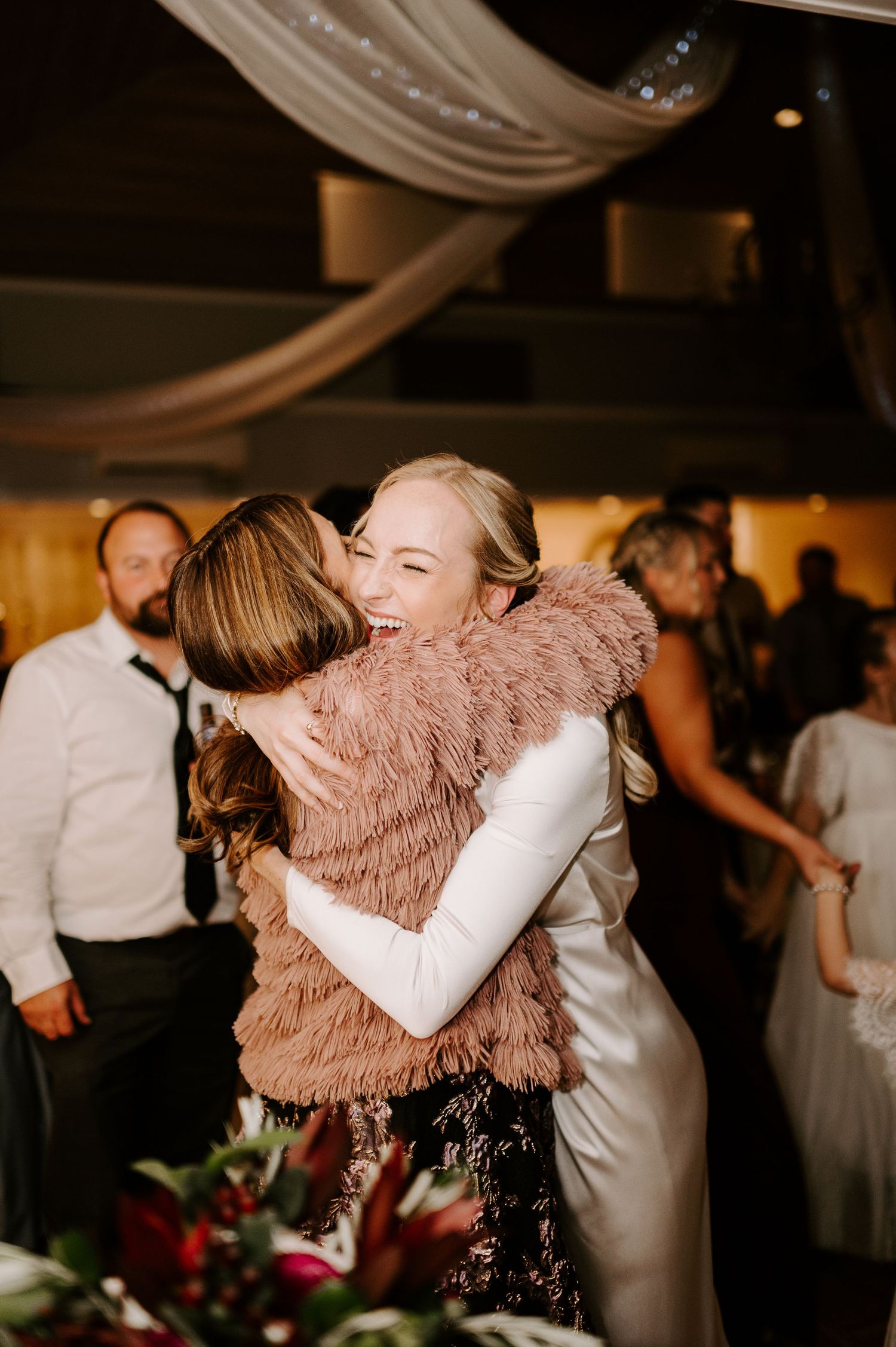 Emotional embrace between wedding guests during reception celebration.