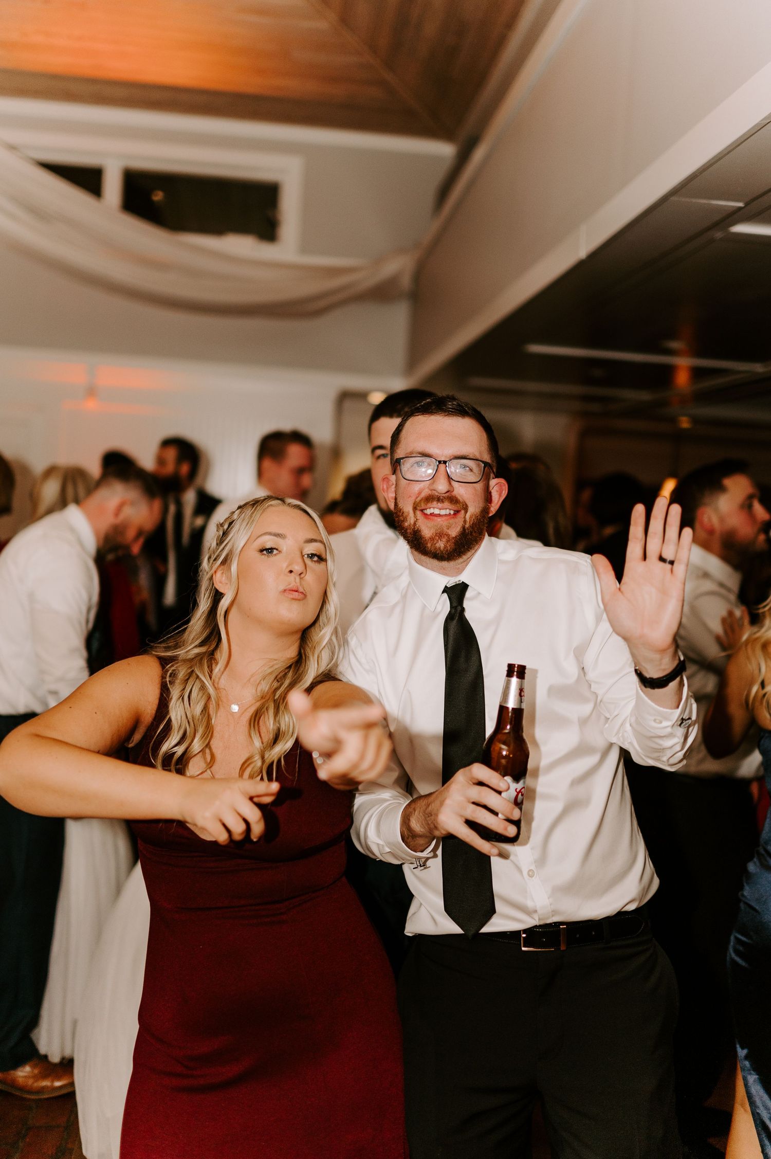 Festive wedding guests dancing and celebrating with drinks at an indoor reception.