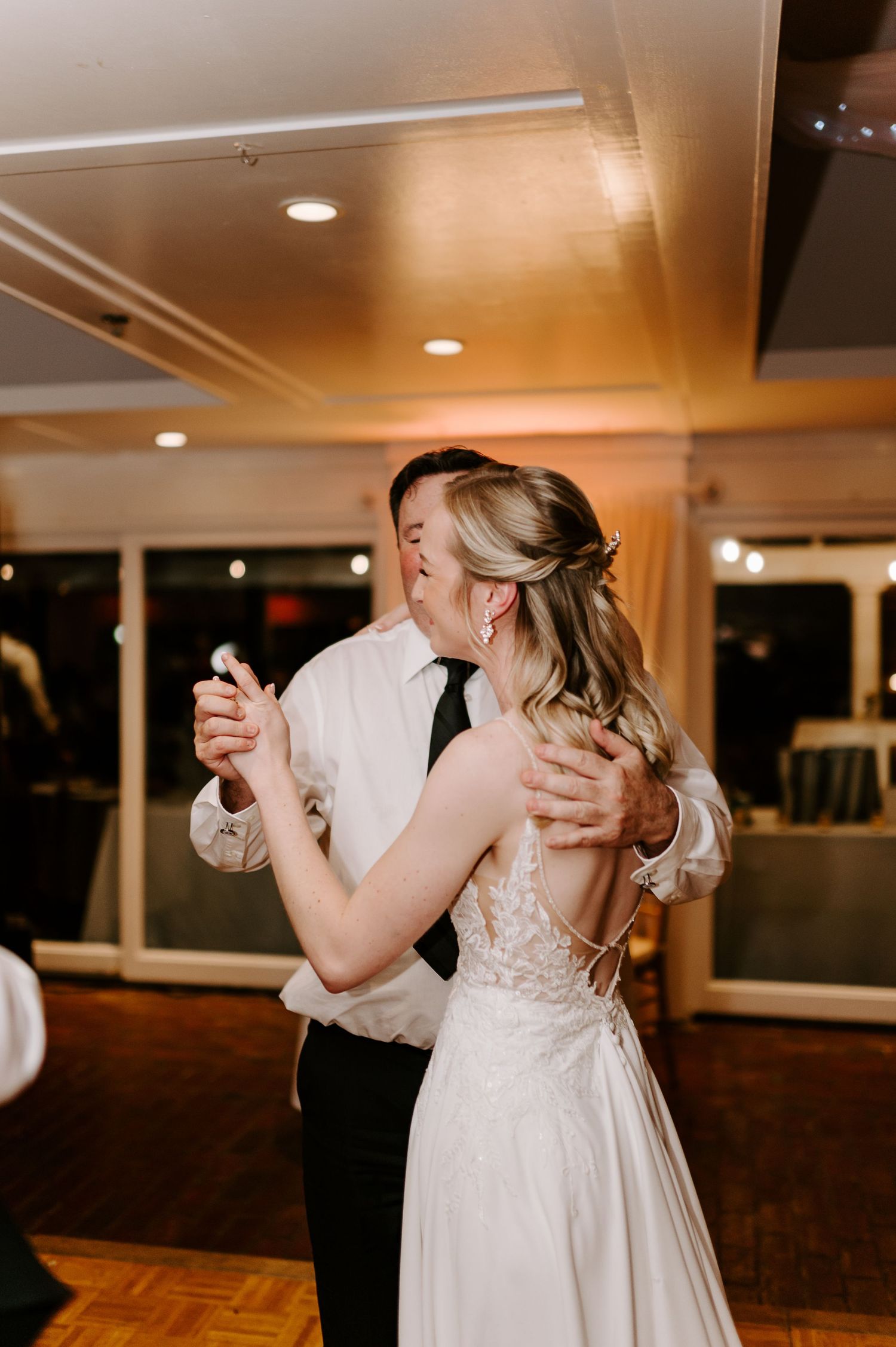 Romantic slow dance moment captured on a wooden dance floor at an indoor reception.