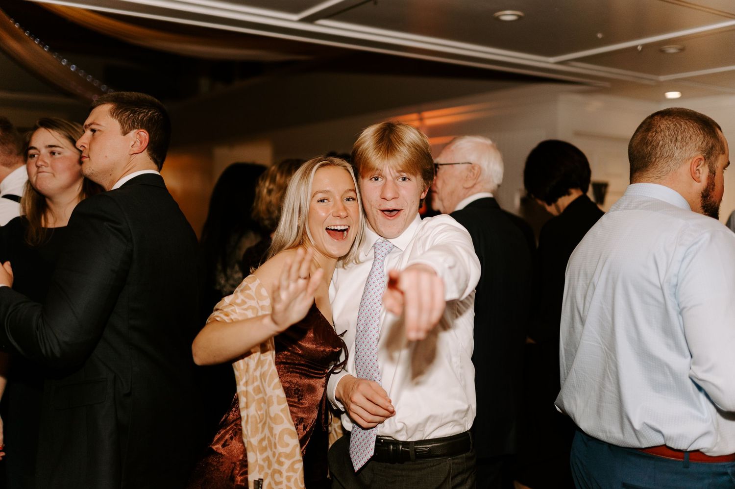 Energetic party guests dancing and laughing during a wedding reception celebration.