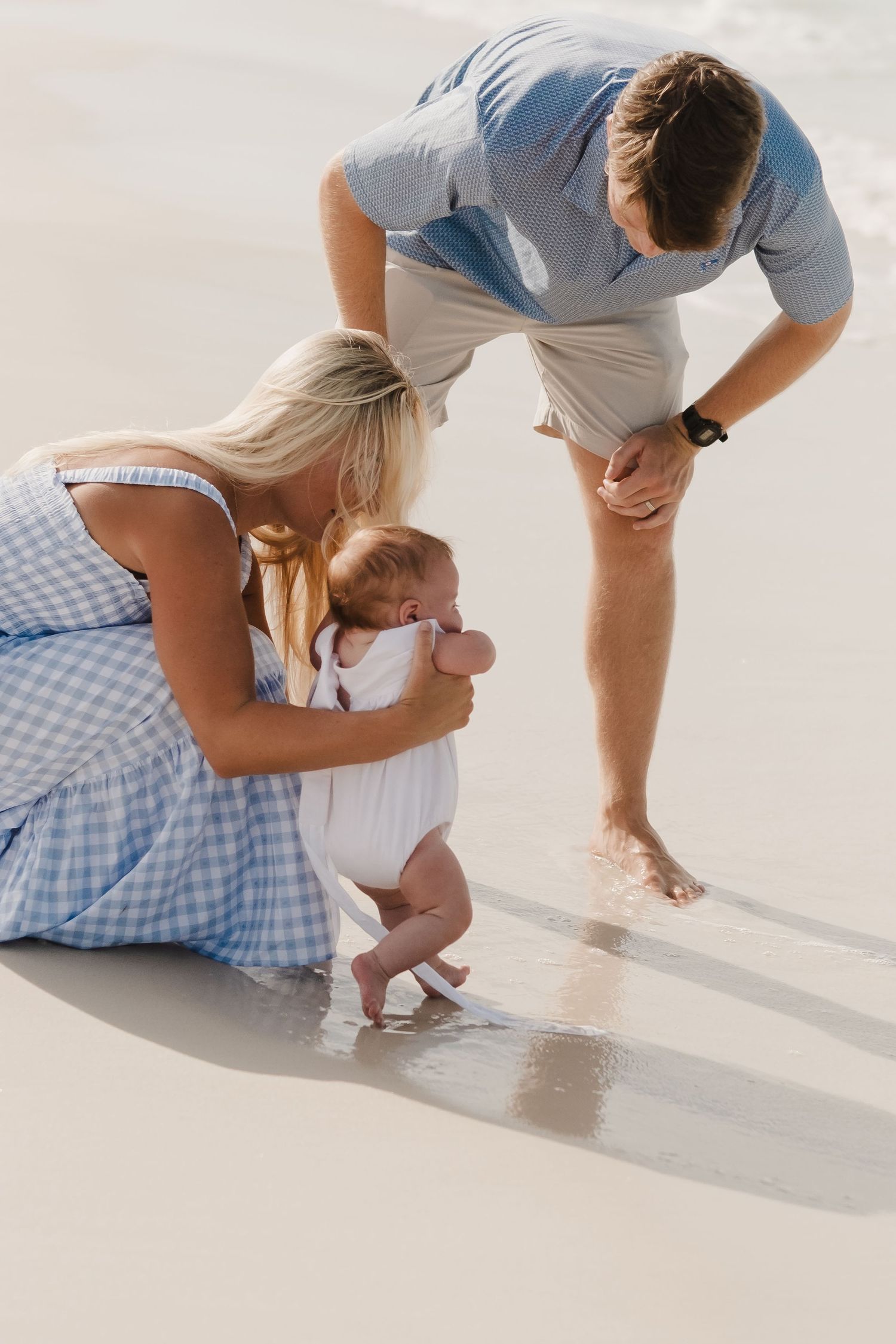 Family in coordinating blue and white outfits playing in beach sand.
