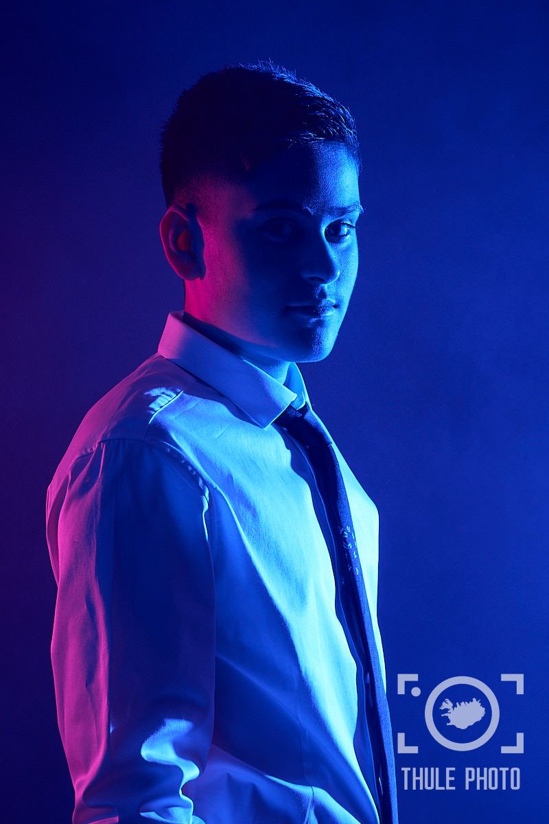Dramatic blue and purple lighting creates moody portrait against dark background.