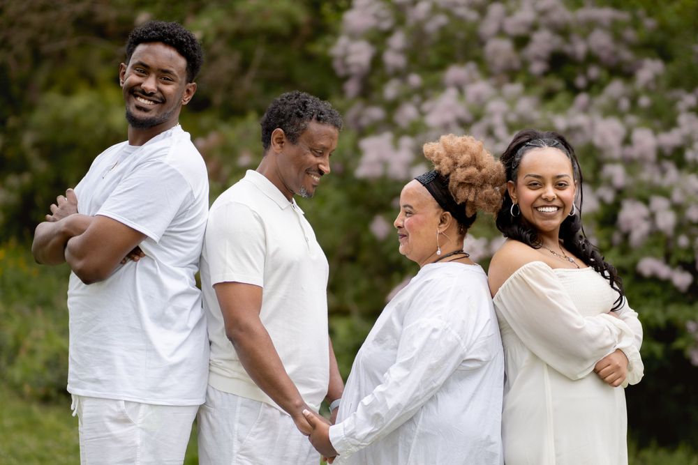 A group of four people pose in coordinated white outfits against a flowering spring background.