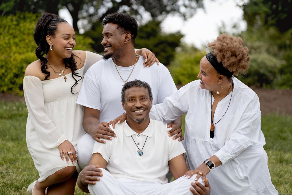 A family shares joyful laughter together while wearing white clothing outdoors in a garden setting.