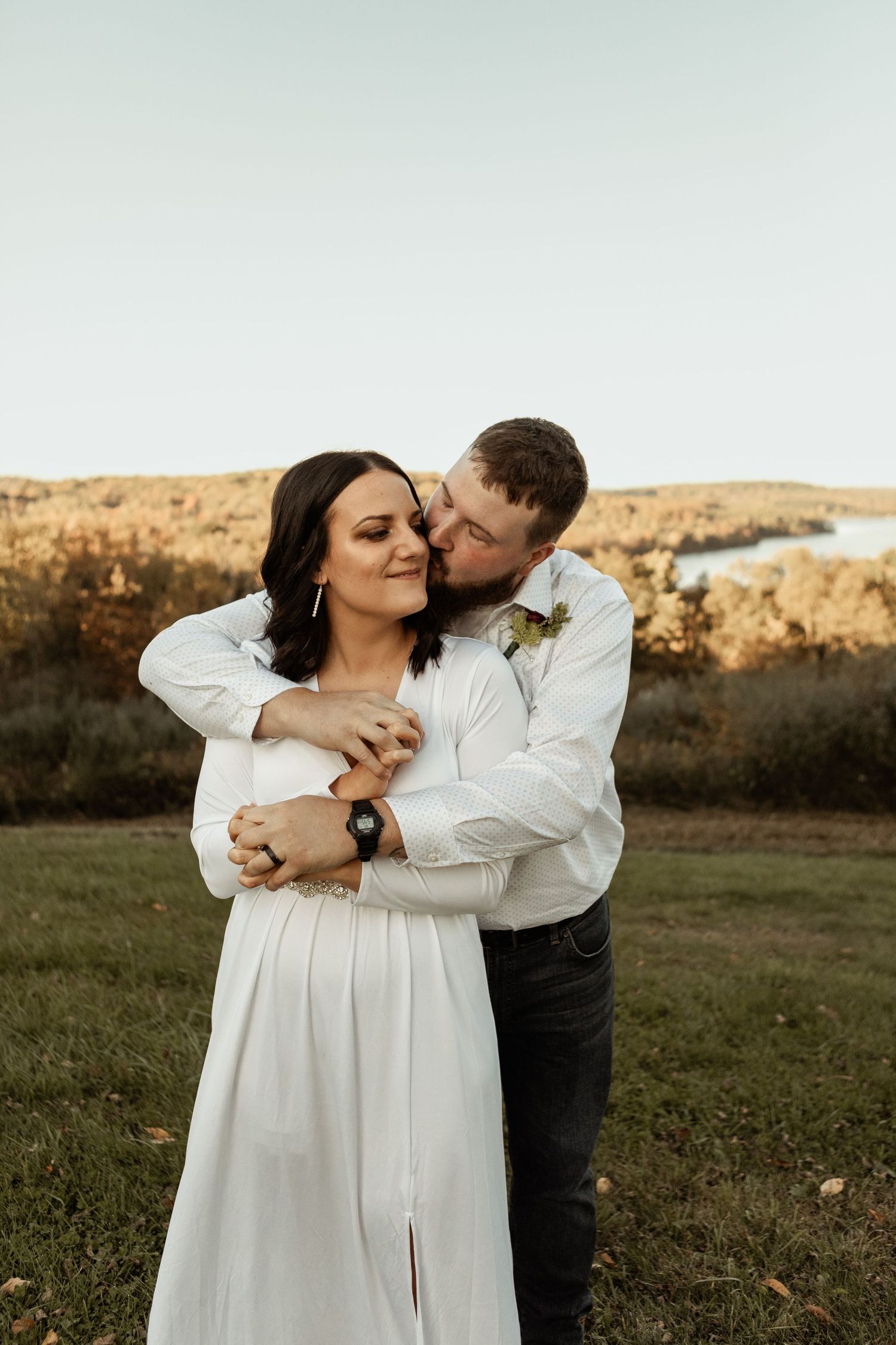A romantic moment between newlyweds embracing in a golden field at sunset.