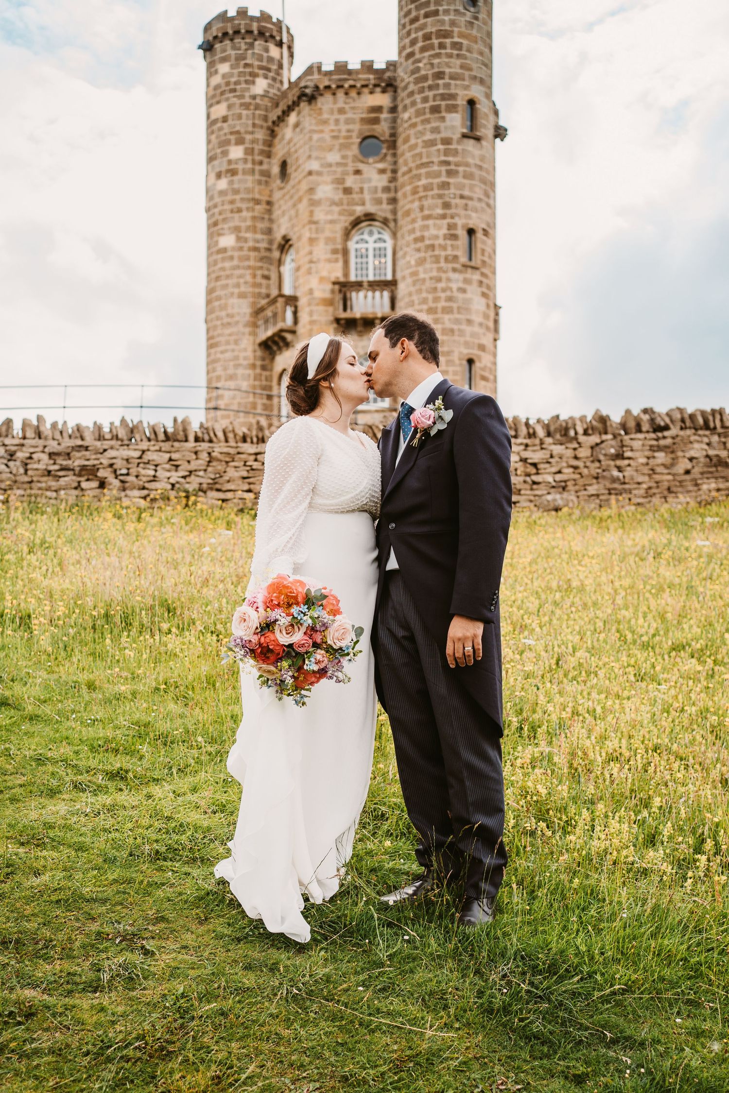 Bride and Groom kissing with tower behind them on a hillside in The Cotswolds