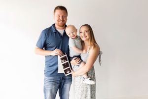 Family pregnancy announcement with sonogram photos in bright white studio setting.
