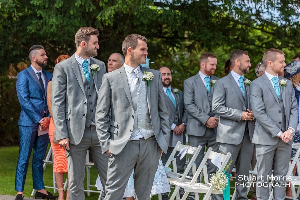 Groom smiling along with wedding guests turn to look at the bride as she walks up the aisle. West tower country house.
