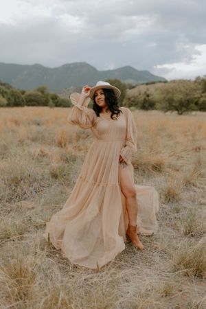 A flowing peach dress dances through desert brush with mountains on the horizon.