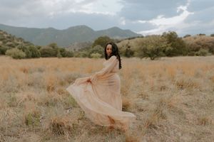 A flowing peach-colored dress billows gracefully against a mountainous desert landscape at sunset.