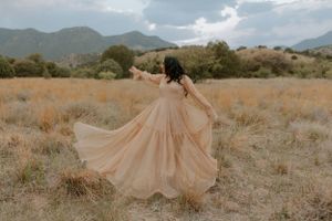 A flowing peach dress creates movement against a backdrop of mountains and desert terrain.