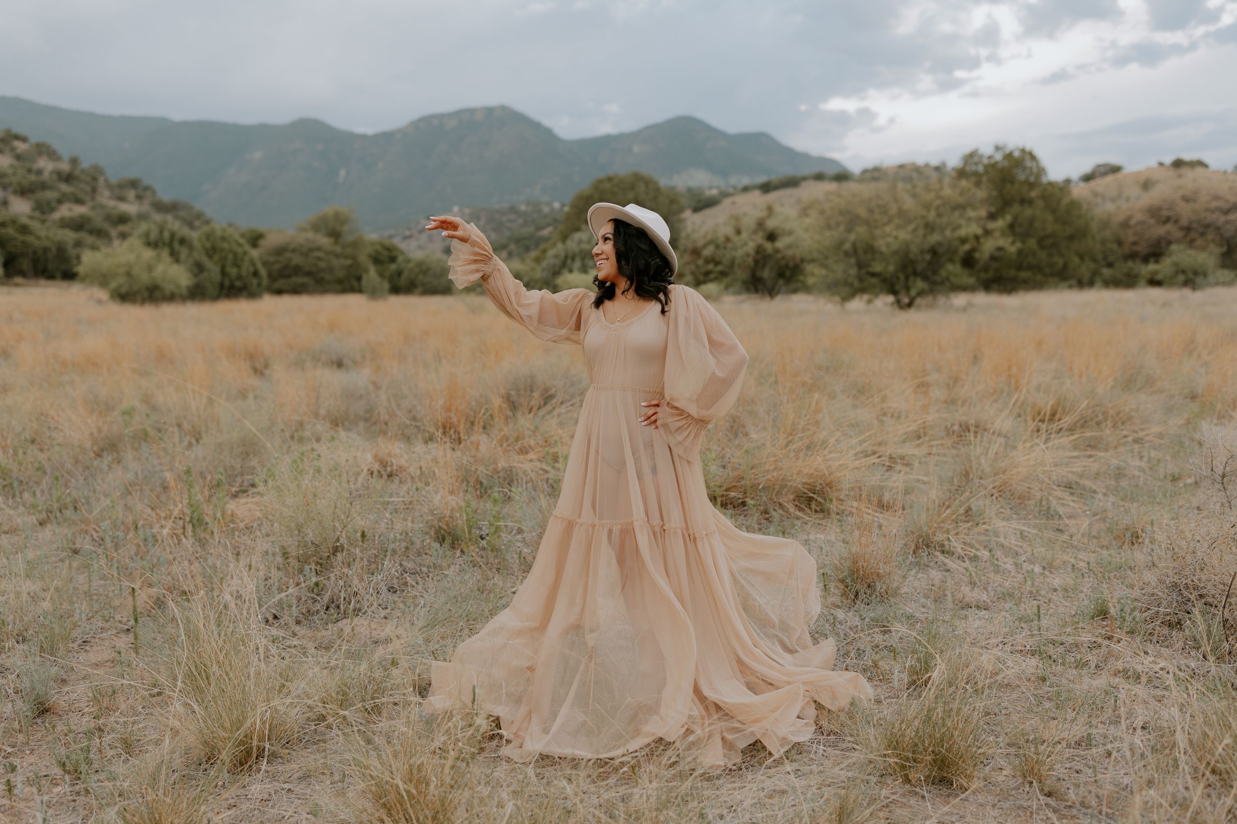 A flowing peach dress moves gracefully across a desert landscape with mountains.