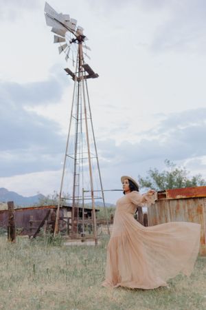 A windswept peach dress creates movement near a vintage windmill in a desert setting.