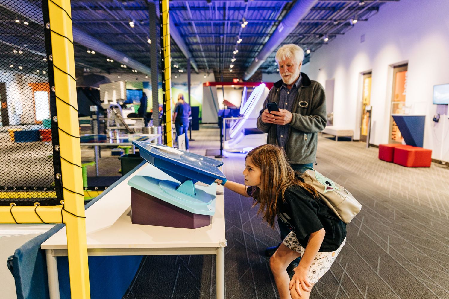 Girl getting ready to launch a paper airplane while grandpa records on his phone at Monroe Science Center