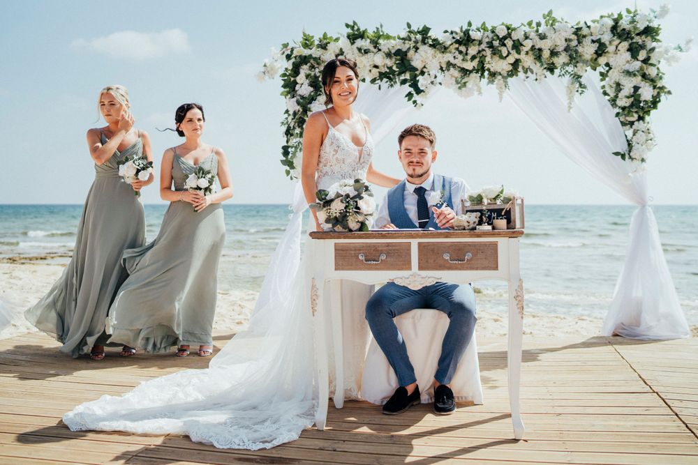 A beach wedding ceremony setup with a white floral arch and decorative table overlooking the ocean.