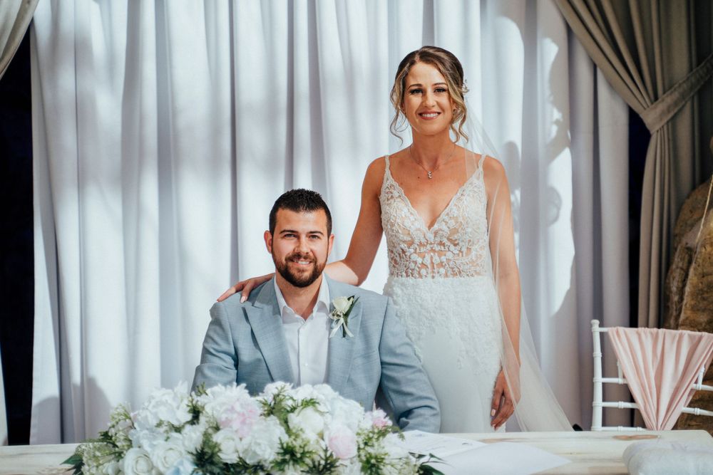 An indoor wedding reception scene with elegant white floral centerpieces and draped curtains.