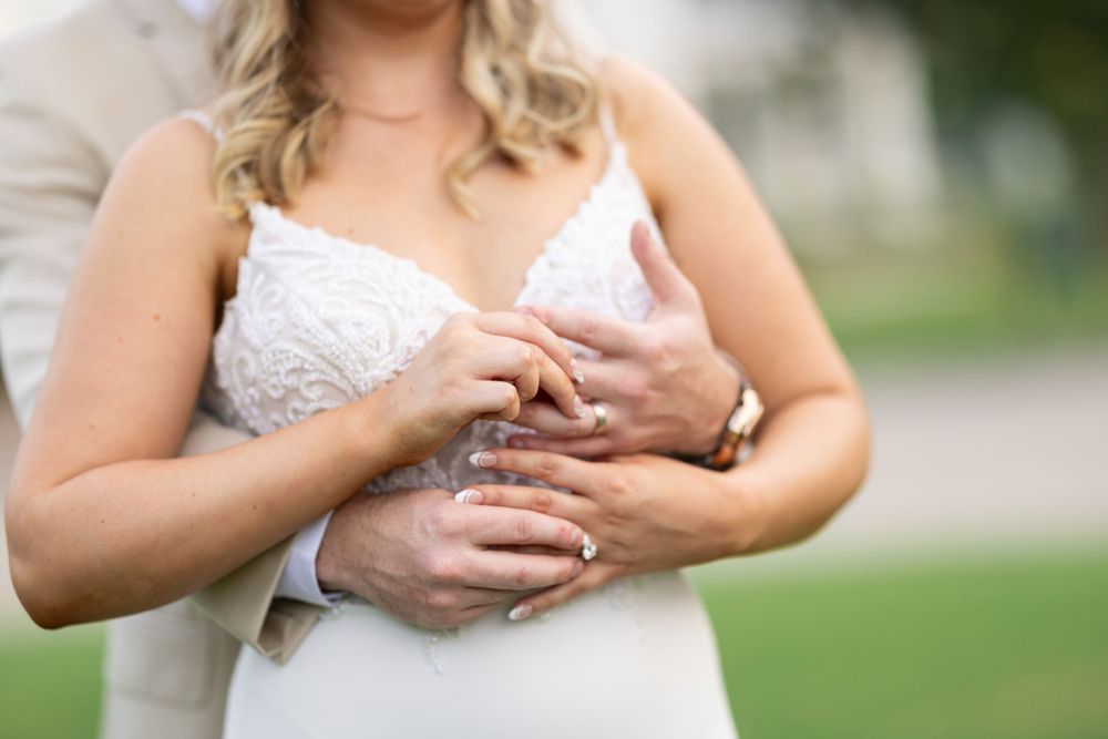 Close-up of wedding rings and hands against a white dress background.