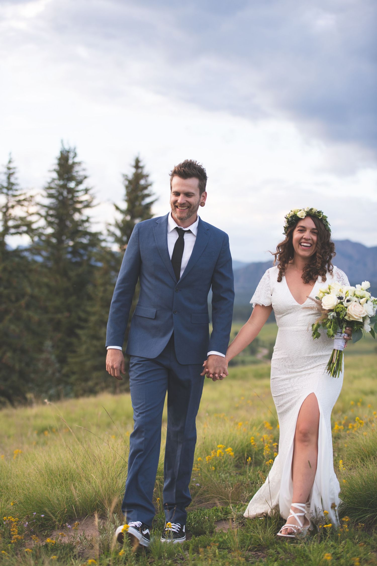 bride and groom holding hands laughing while walking in from the mountains and forest