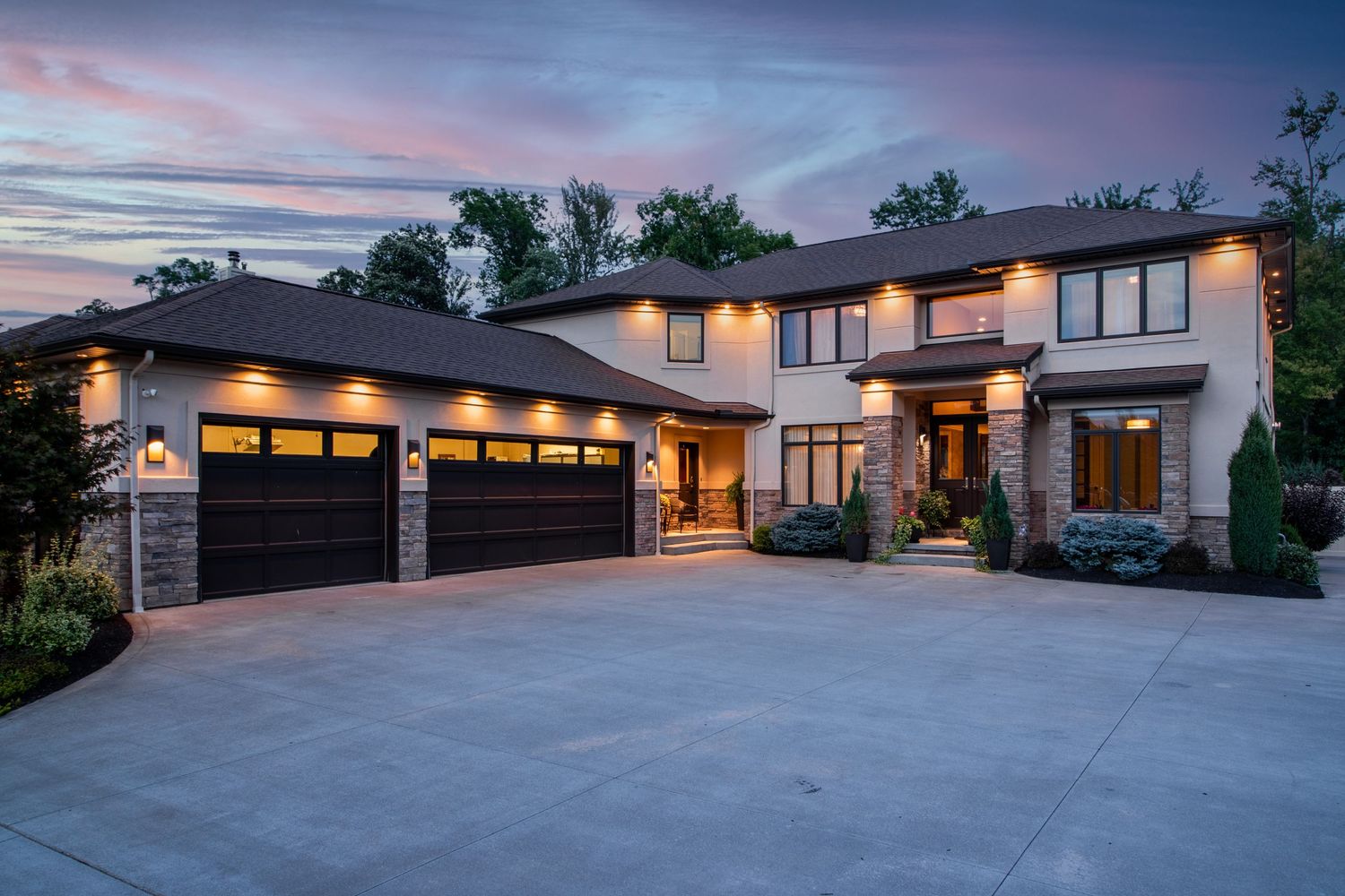 Contemporary luxury home exterior at dusk with illuminated garage doors and modern architecture.