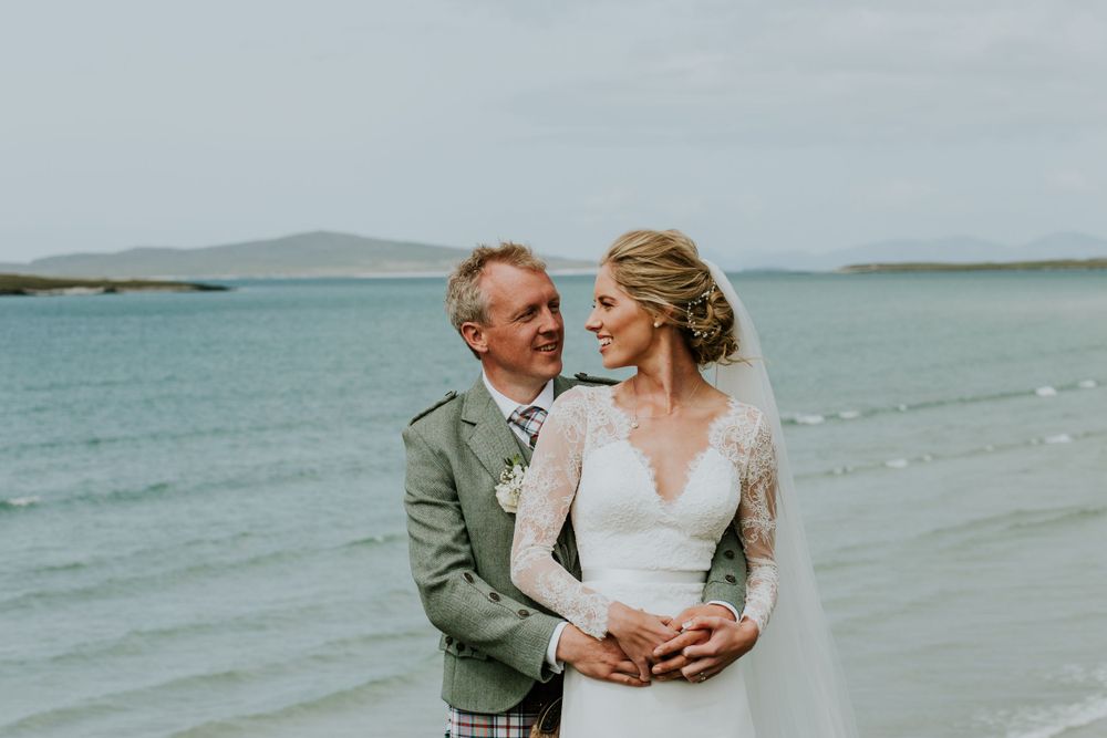Intimate beach wedding portrait with couple embracing against turquoise ocean backdrop.